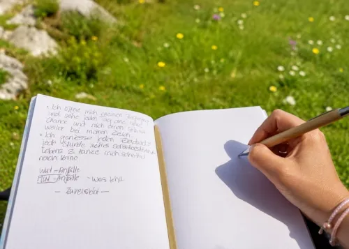Hand beim Schreiben in einem Notizbuch auf einer Wiese