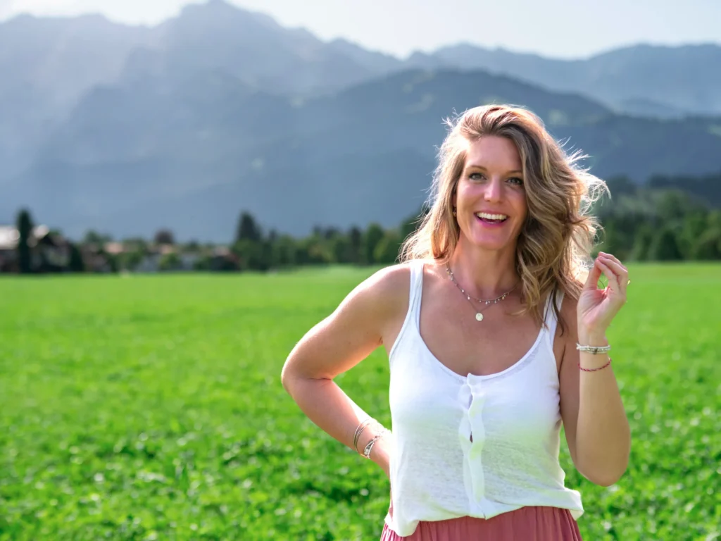 Lächelnde Frau auf einer grünen Wiese vor einer Berglandschaft